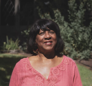 African-American Woman in foreground with trees in background on a sunny day.